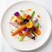 Assiette de haute gastronomie française vue de dessus, ornée de légumes colorés délicatement disposés, de fines touches de sauce et de micro pousses sous une lumière douce.